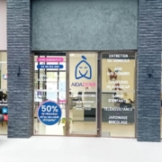 Une devanture aux larges vitres affiche le logo d'AIDADOM et la liste des services en français : soins à domicile, aide aux personnes âgées, accompagnement du handicap, ménage, jardinage, téléassistance. Du mobilier de bureau est visible à l'intérieur.
