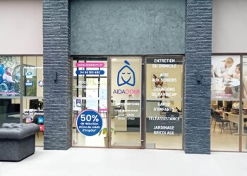 Une devanture aux larges vitres affiche le logo d'AIDADOM et la liste des services en français : soins à domicile, aide aux personnes âgées, accompagnement du handicap, ménage, jardinage, téléassistance. Du mobilier de bureau est visible à l'intérieur.