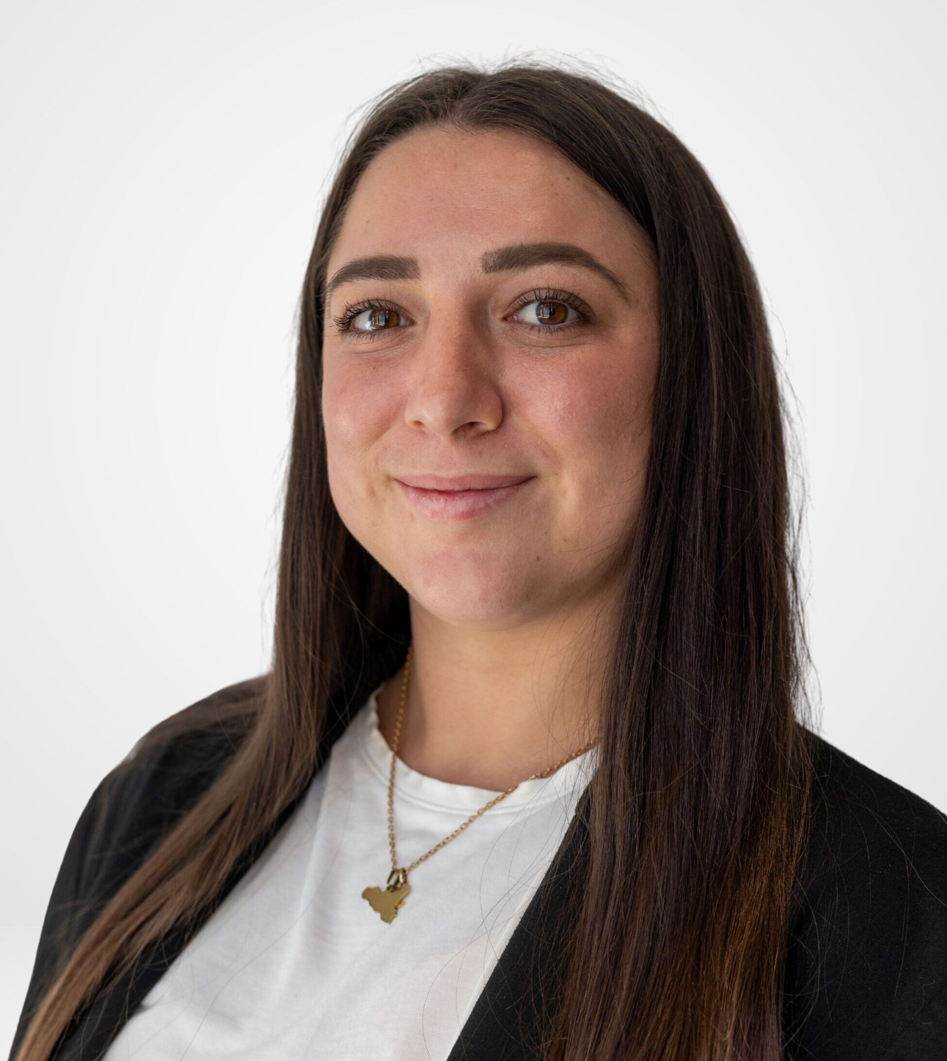 Une jeune femme souriante aux longs cheveux foncés, vêtue d'un t-shirt blanc, d'un blazer noir et d'un collier en or.