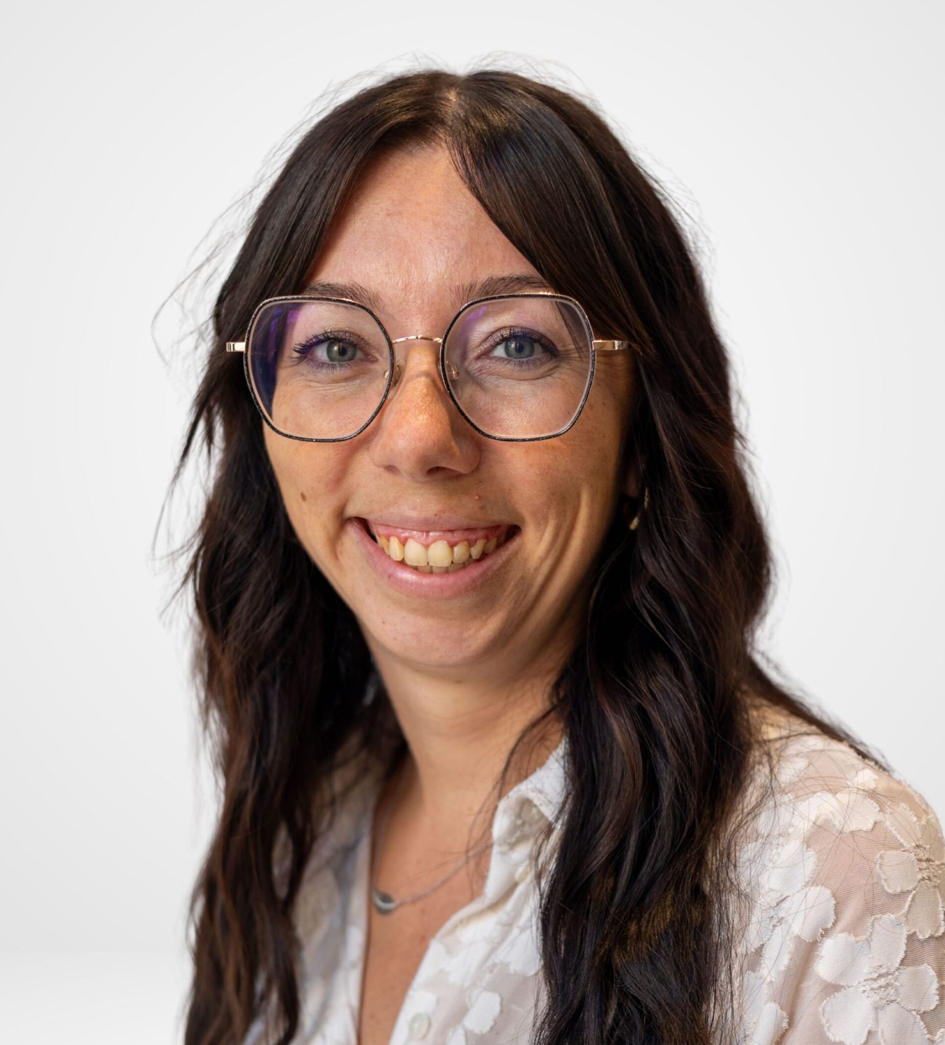 Une femme aux longs cheveux bruns, portant des lunettes, qui sourit à la caméra.