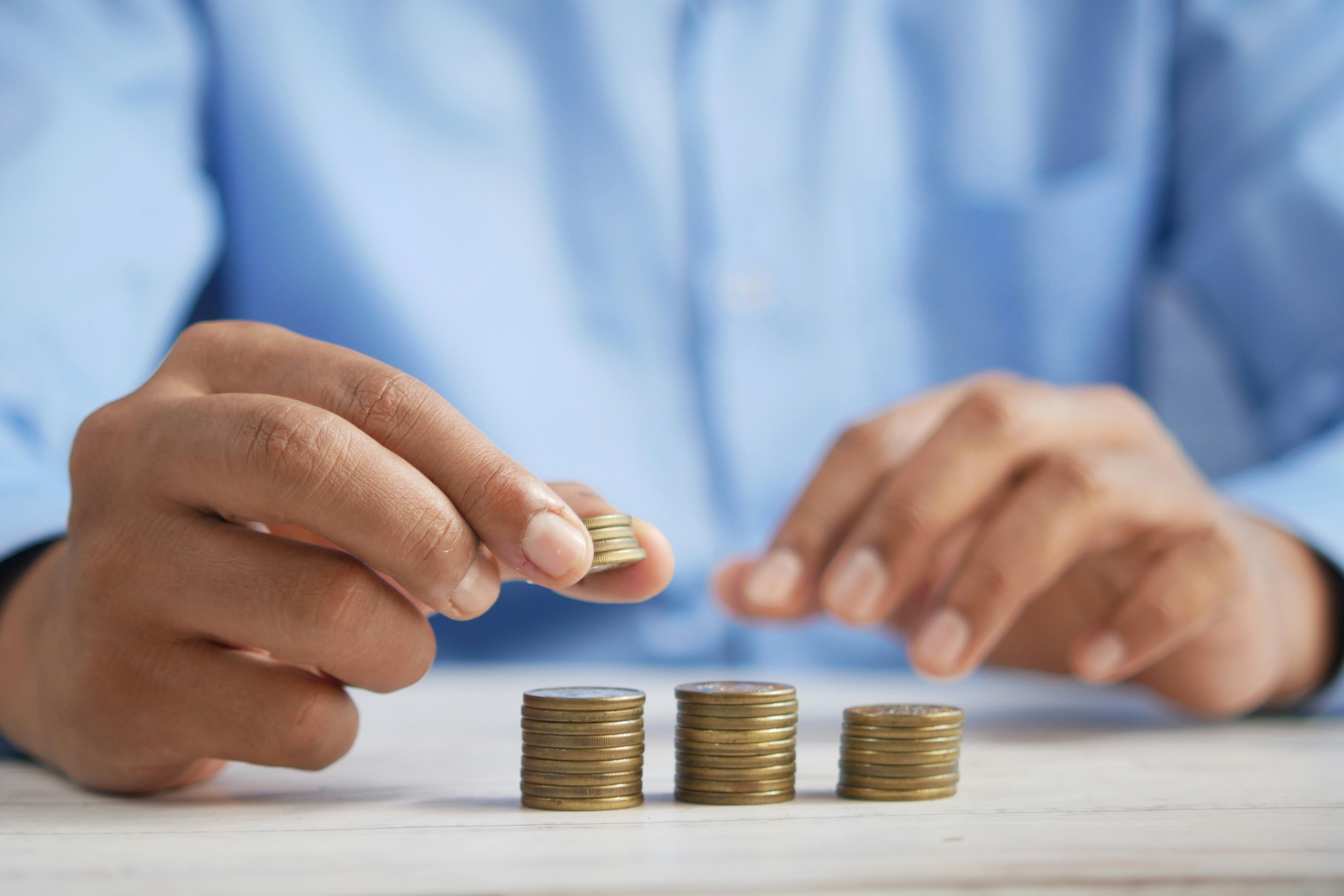 Une personne en chemise bleue empile des pièces de monnaie sur une surface blanche, illustrant les économies possibles avec les services à la personne -50% grâce à l'avance immédiate crédit d'impôt.