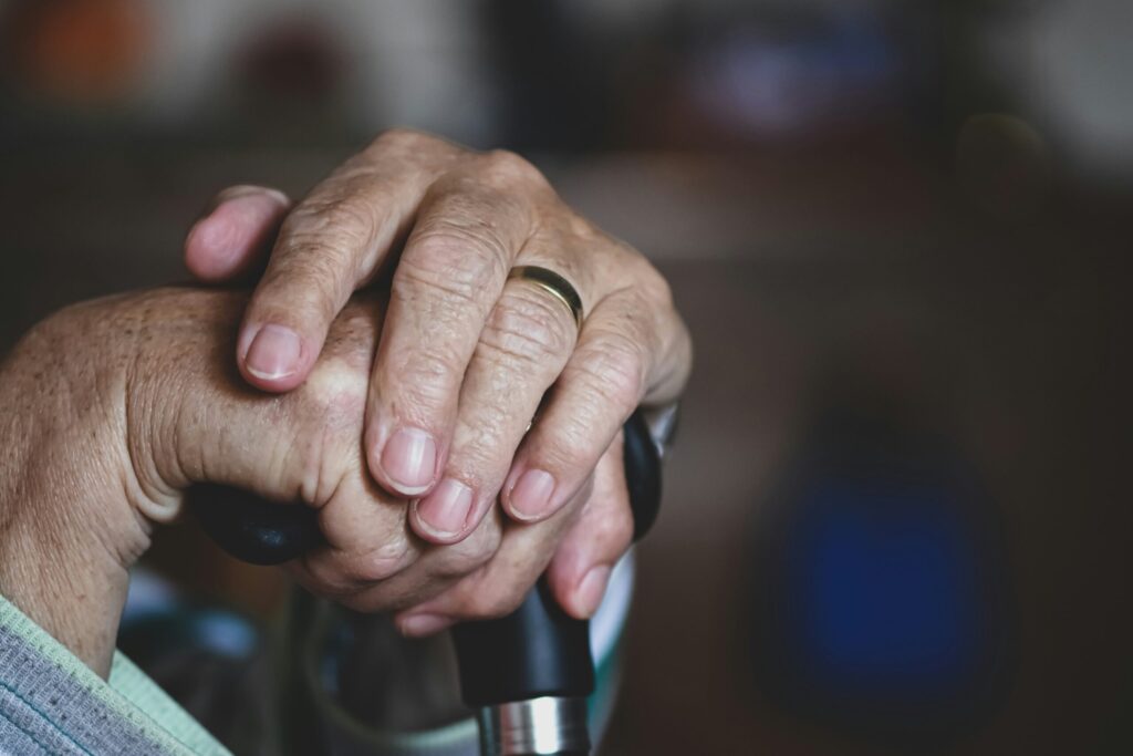 Gros plan sur les mains d'une personne âgée reposant sur une canne, une bague en or brillant à un doigt. L'image évoque l'âge, le soutien et la contemplation, reflétant les moments où l'aide ménagère du CESU peut apporter confort et indépendance.