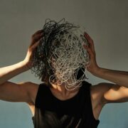 Une personne vêtue d'une chemise noire sans manches tient devant son visage une masse enchevêtrée de fils noirs et blancs - comme les 10 erreurs qui vous font perdre le fil - qui masquent ses traits, sur un fond uni.