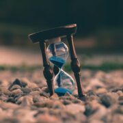 Un sablier de sable bleu, symbolisant le passage du temps, repose sur des pierres lisses, nous rappelant que des erreurs de nettoyage peuvent se produire si nous nous précipitons dans nos tâches quotidiennes dans un cadre naturel.