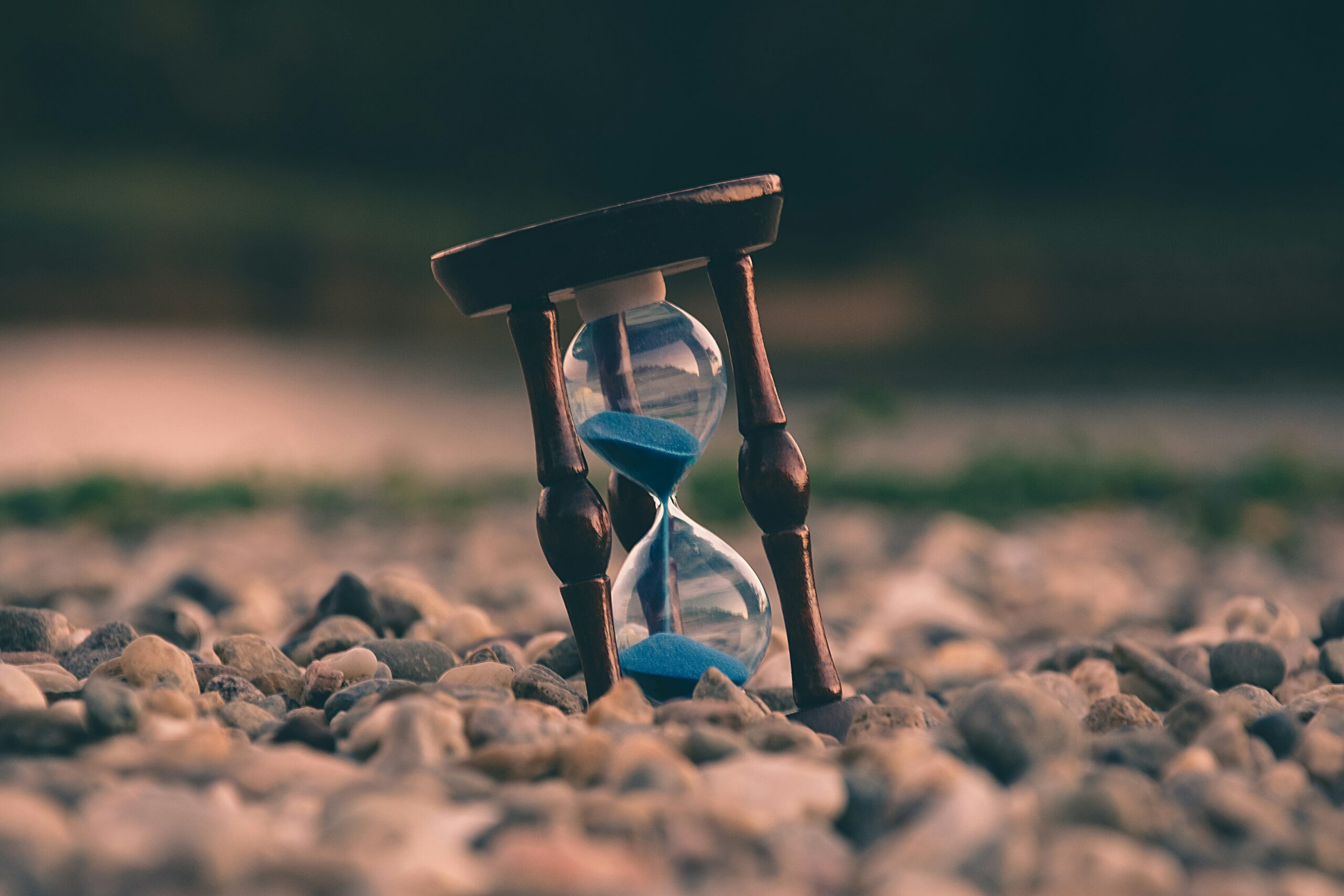 Un sablier de sable bleu, symbolisant le passage du temps, repose sur des pierres lisses, nous rappelant que des erreurs de nettoyage peuvent se produire si nous nous précipitons dans nos tâches quotidiennes dans un cadre naturel.