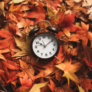 Un réveil noir indiquant 2 h 54 est entouré d’un tas de feuilles d’automne aux nuances d’orange, de rouge et de marron — un rappel saisissant de la date du changement d’heure de 2026.