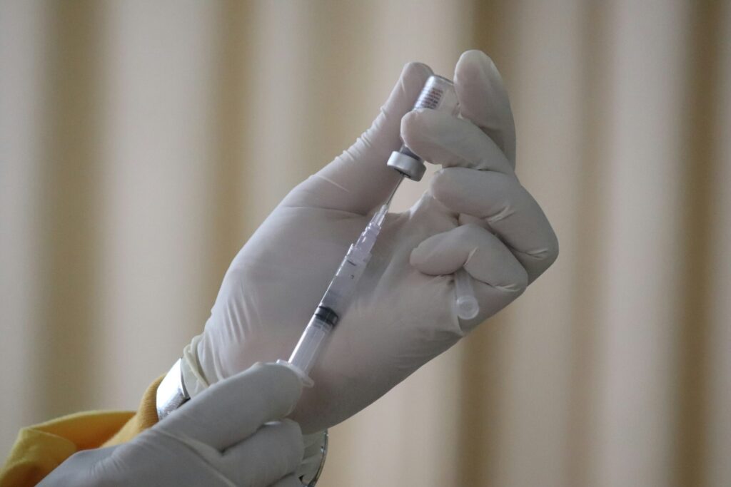 Une personne portant des gants médicaux blancs prélève le vaccin contre la grippe 2026 d'un flacon pour le mettre dans une seringue.