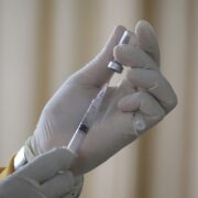 Une personne portant des gants médicaux blancs prélève le vaccin contre la grippe 2026 d'un flacon pour le mettre dans une seringue.