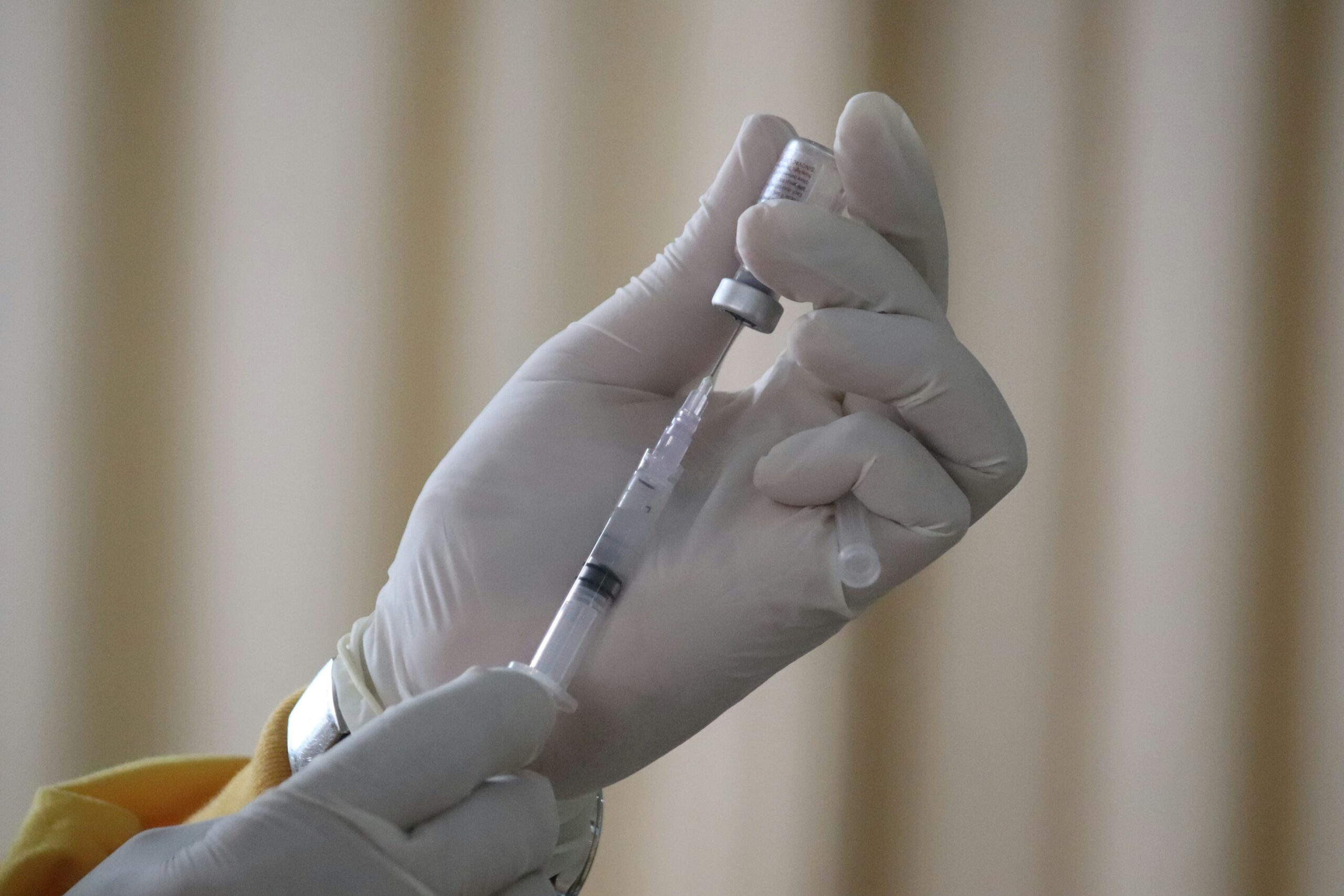 Une personne portant des gants médicaux blancs prélève le vaccin contre la grippe 2026 d'un flacon pour le mettre dans une seringue.