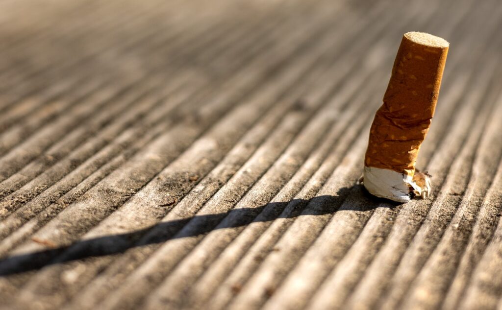 Un mégot de cigarette jeté se dresse sur une surface en bois, projetant une longue ombre, formant un contraste saisissant avec une maison propre et bien rangée par une aide ménagère à domicile bénéficiant du crédit d’impôt.