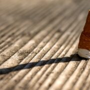 Un mégot de cigarette jeté se dresse sur une surface en bois, projetant une longue ombre, formant un contraste saisissant avec une maison propre et bien rangée par une aide ménagère à domicile bénéficiant du crédit d’impôt.