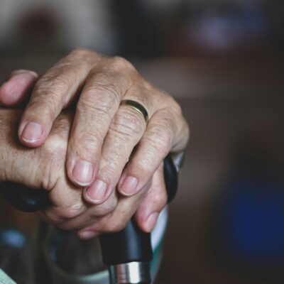 Gros plan sur les mains d'une personne âgée reposant sur une canne, une bague en or brillant à un doigt. L'image évoque l'âge, le soutien et la contemplation, reflétant les moments où l'aide ménagère du CESU peut apporter confort et indépendance.