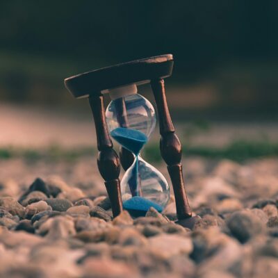 Un sablier de sable bleu, symbolisant le passage du temps, repose sur des pierres lisses, nous rappelant que des erreurs de nettoyage peuvent se produire si nous nous précipitons dans nos tâches quotidiennes dans un cadre naturel.