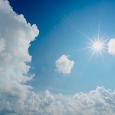 Soleil brillant dans un ciel bleu clair avec des nuages blancs épars, certains paraissant cotonneux et larges, créant une scène diurne vibrante et sereine.