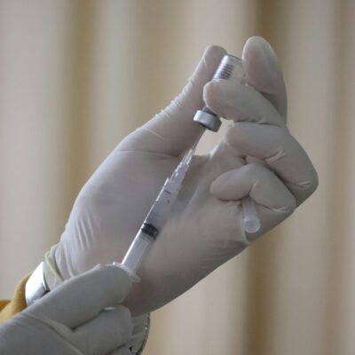 Une personne portant des gants médicaux blancs prélève le vaccin contre la grippe 2026 d'un flacon pour le mettre dans une seringue.
