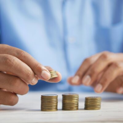 Une personne en chemise bleue empile des pièces de monnaie sur une surface blanche, illustrant les économies possibles avec les services à la personne -50% grâce à l'avance immédiate crédit d'impôt.
